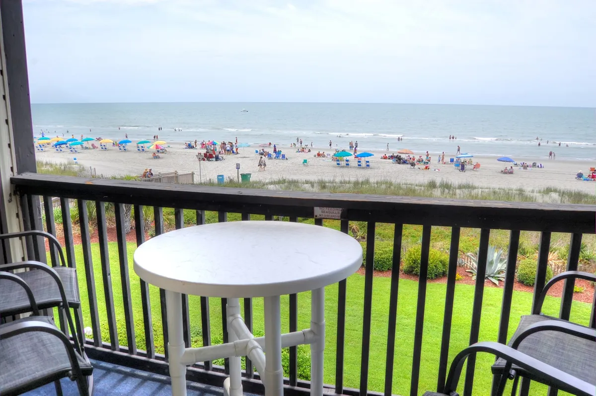 A stunning beachfront setup with ocean views, umbrellas, a table and chairs arranged for relaxation or dining just steps from the sand. The inviting atmosphere highlights easy beach access and spaces for social gatherings or peaceful escapes.