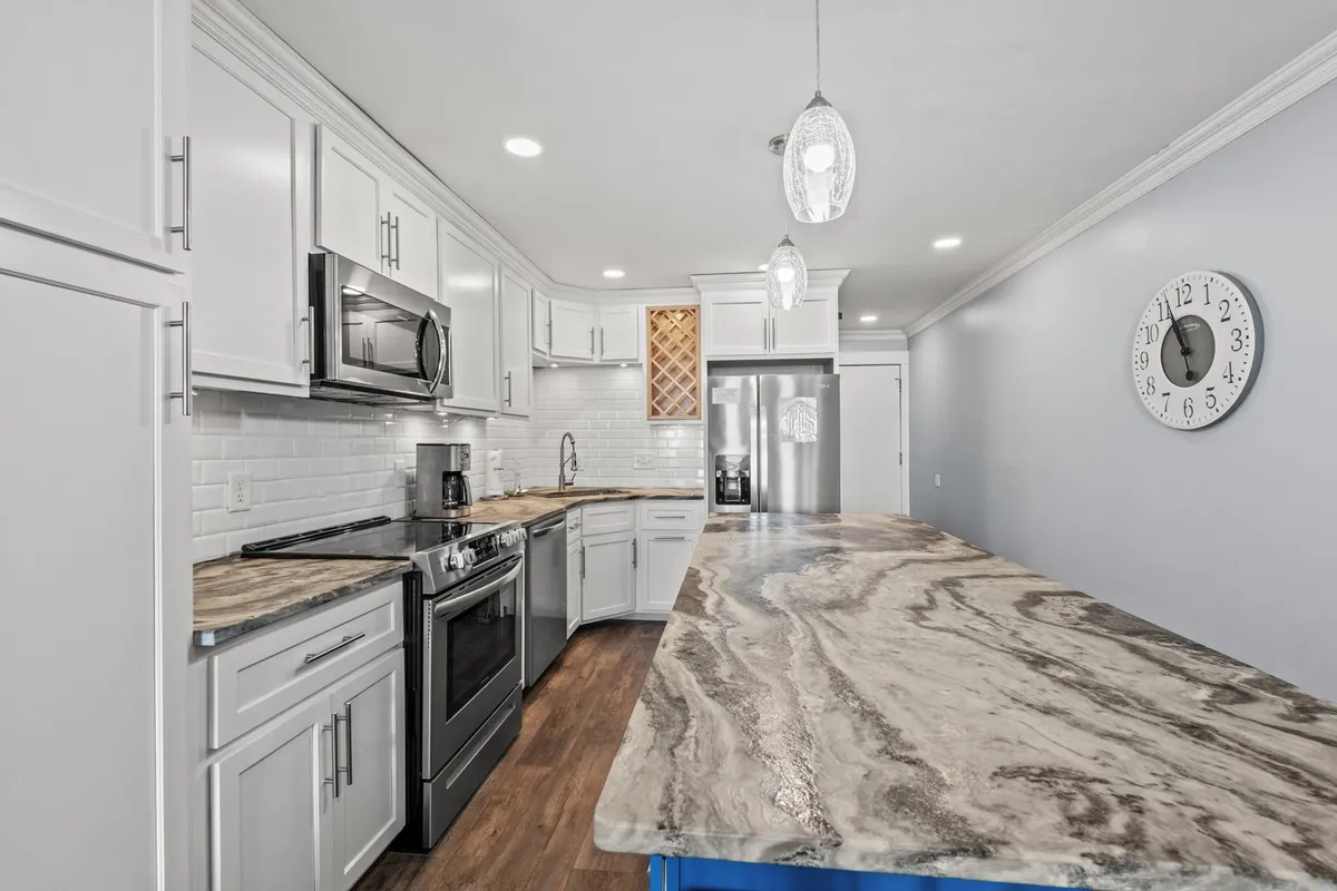 A spacious, modern kitchen with a central island, stainless steel appliances, granite countertops, and stylish pendant lights. The setup suggests a welcoming environment for both cooking and socializing, with ample counter space for meal prep and entertaining.