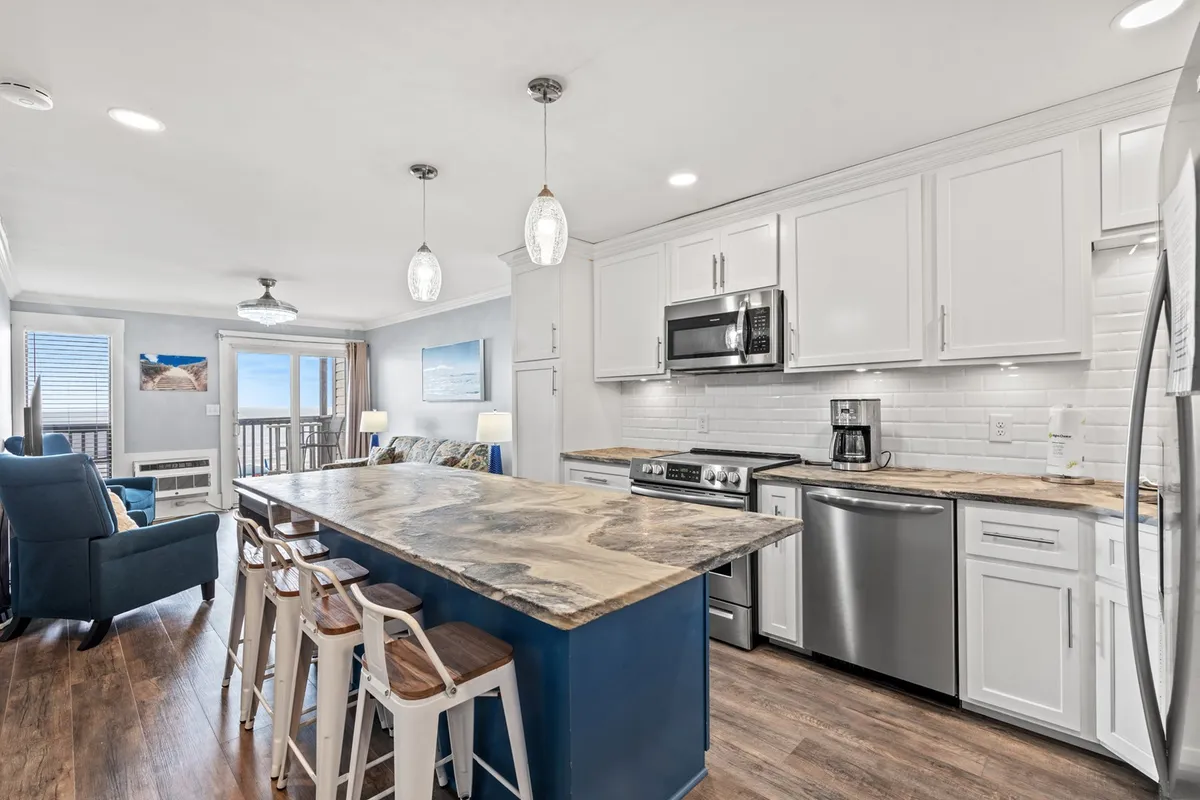 A welcoming, open-plan space highlighted by a large kitchen island, comfortable seating area, and floor-to-ceiling windows that frame a stunning ocean view. The setup invites guests to gather, dine, or socialize while enjoying natural light and the calming effect of the sea beyond.