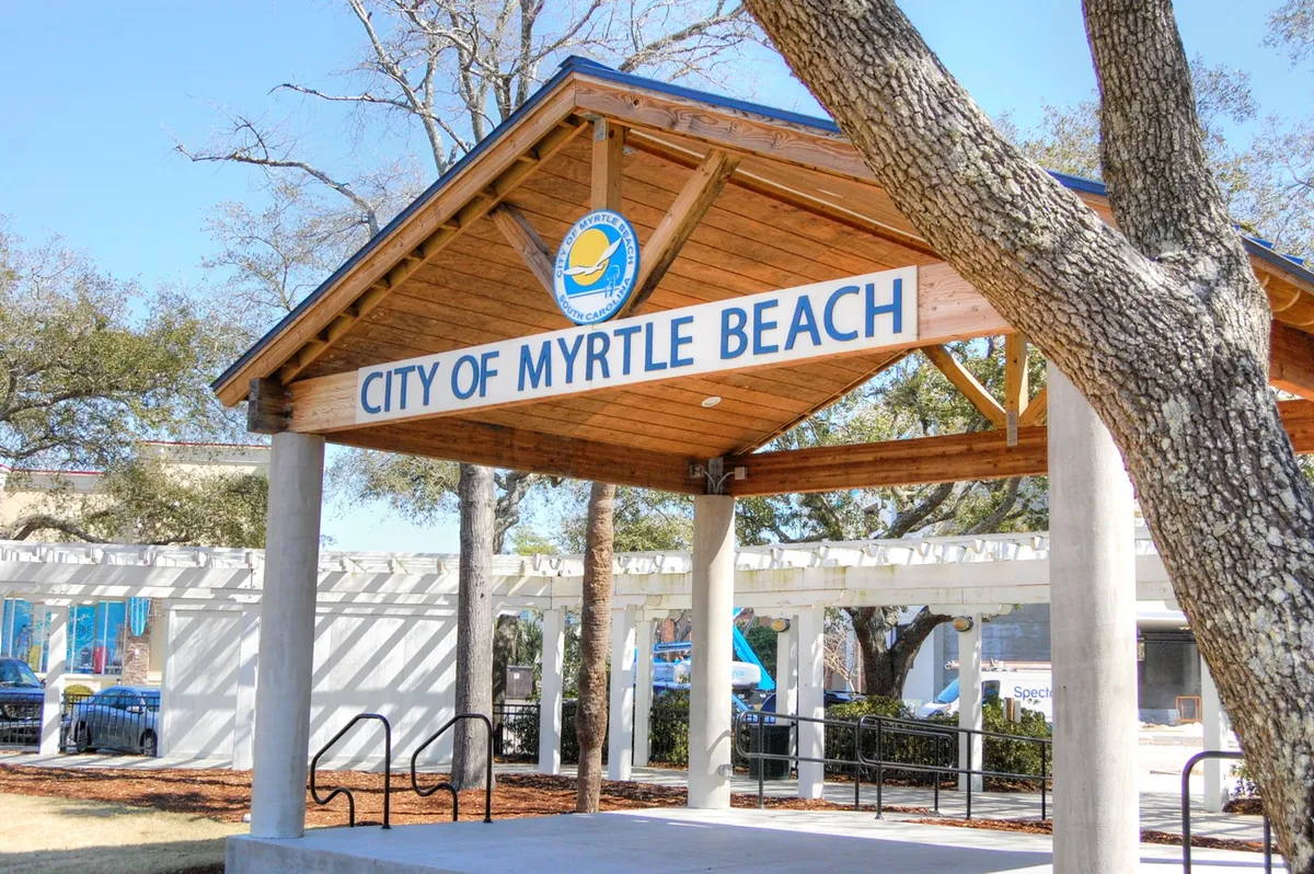 A welcoming wooden structure with the signage 'CITY OF MYRTLE BEACH,' surrounded by trees. The scene invites viewers into a space that hosts community events and gatherings, reflecting the area's local charm.